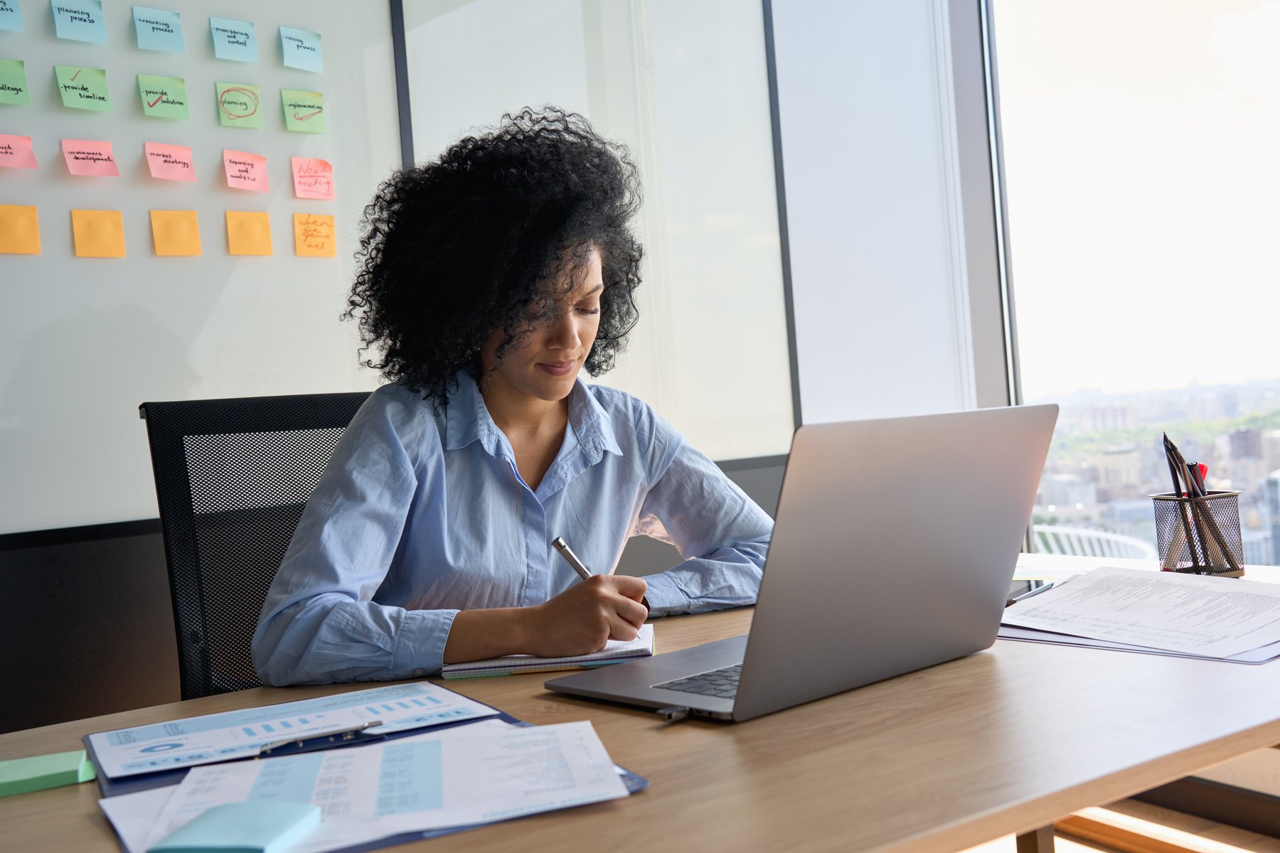 Concentrated African American Data Analyst Working Using Pc Writing Notes.